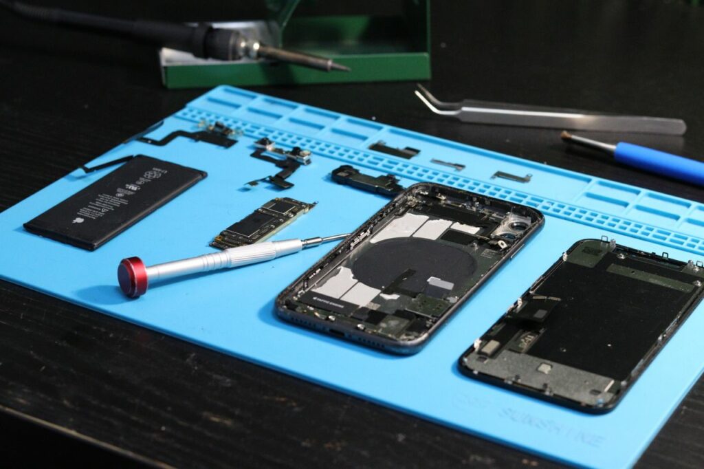 Close-up of disassembled smartphone parts on a blue repair mat with tools.