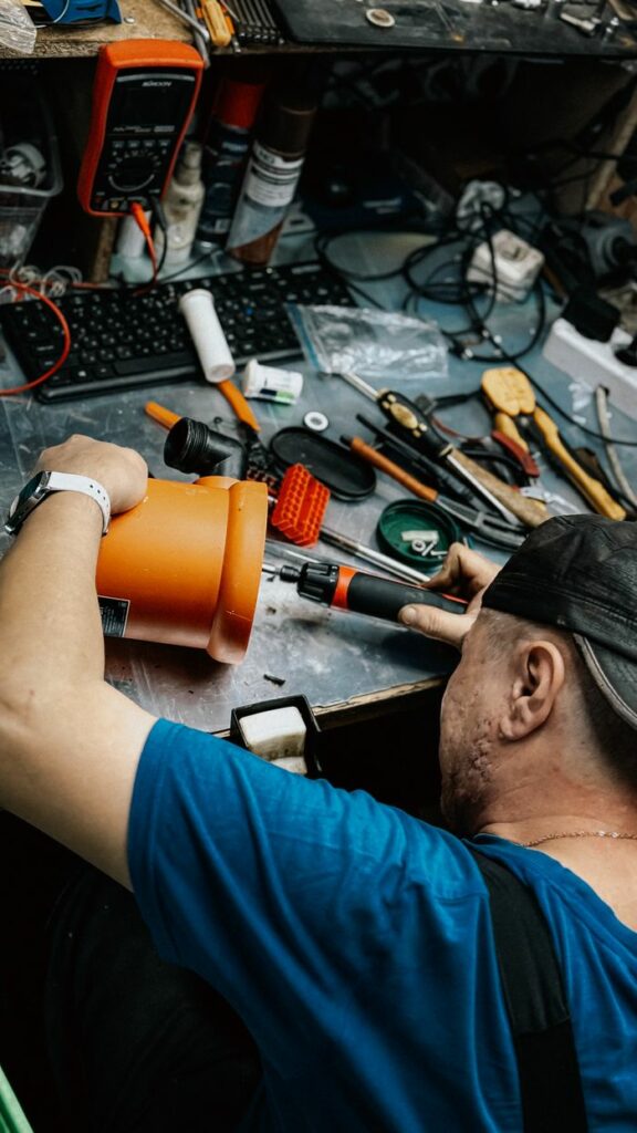 A technician repairing electronic equipment amidst various tools and gadgets in a messy workshop.